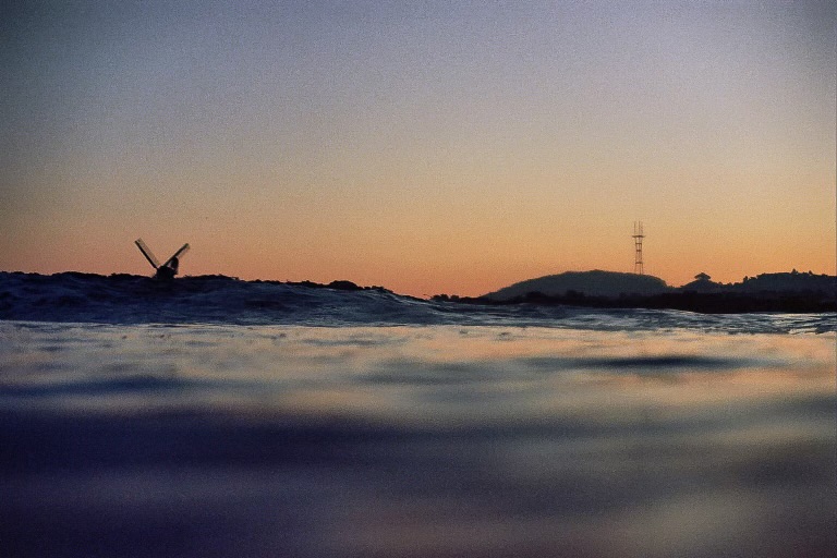 A calm sunset over a body of water with a distant windmill on the left and a radio tower on a hill to the right.