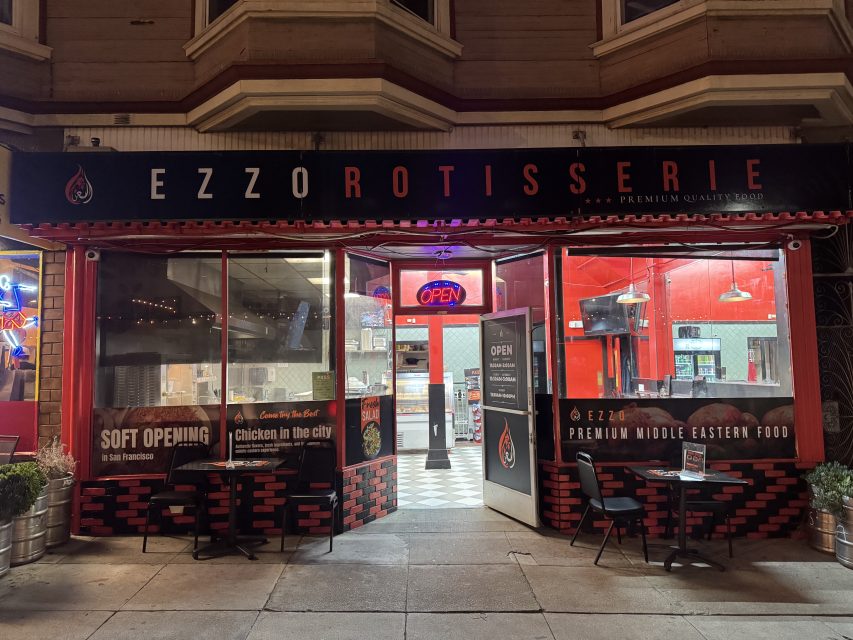 Street view of Ezzo Rotisserie, a Middle Eastern restaurant with an open sign, outdoor seating, and banners announcing a soft opening in San Francisco.