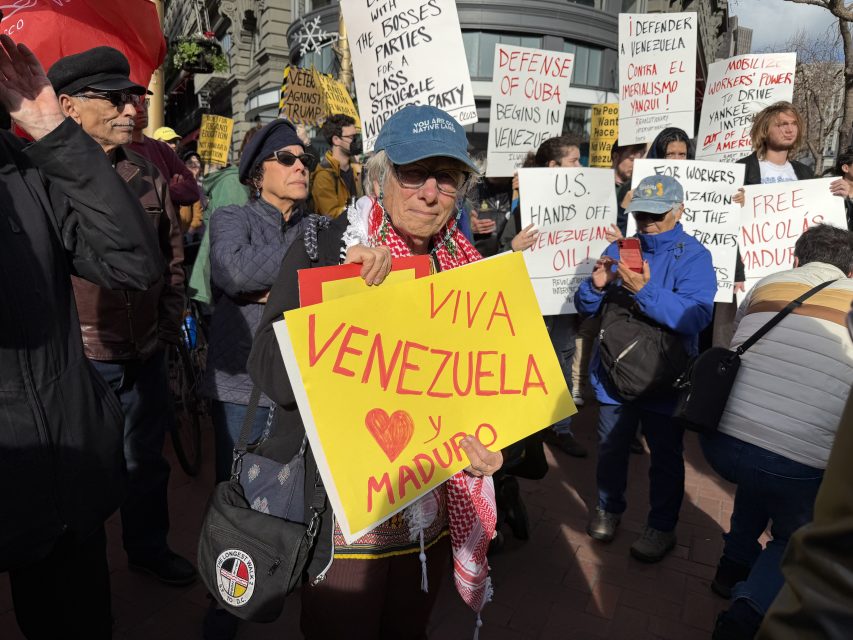 A group of protesters hold signs supporting Venezuela and Nicolás Maduro, with one person prominently displaying a yellow "Viva Venezuela y Maduro" sign.
