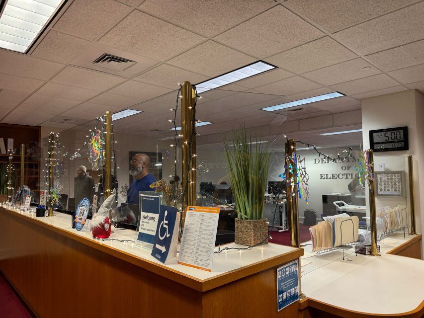 Office reception area with glass dividers and decorative lights, inspired by the calm of Sunset Dunes. Staff members are behind the counter near an analog clock at 5:00, with files and plants on display, echoing Great Highway’s modern touch.
