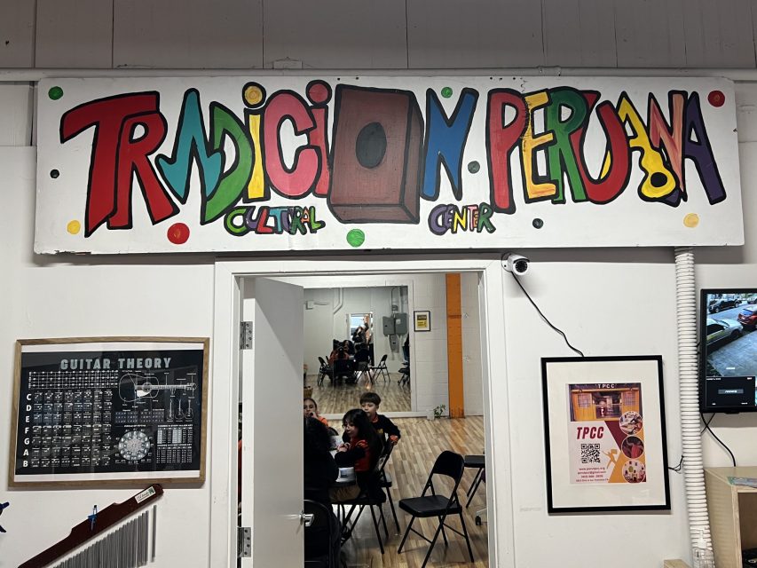 A colorful sign reading "Tradicion Peruana Cultural Center" hangs above an open doorway; people are seated inside, and framed posters and a TV are on the walls.