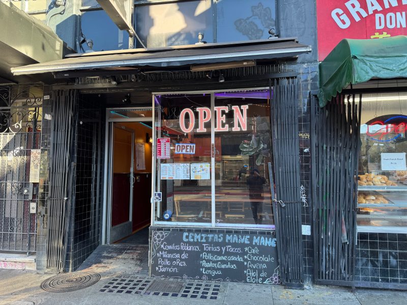 Street view of a small restaurant with an "OPEN" sign in the window; menu items are listed in Spanish on a chalkboard below the front window.