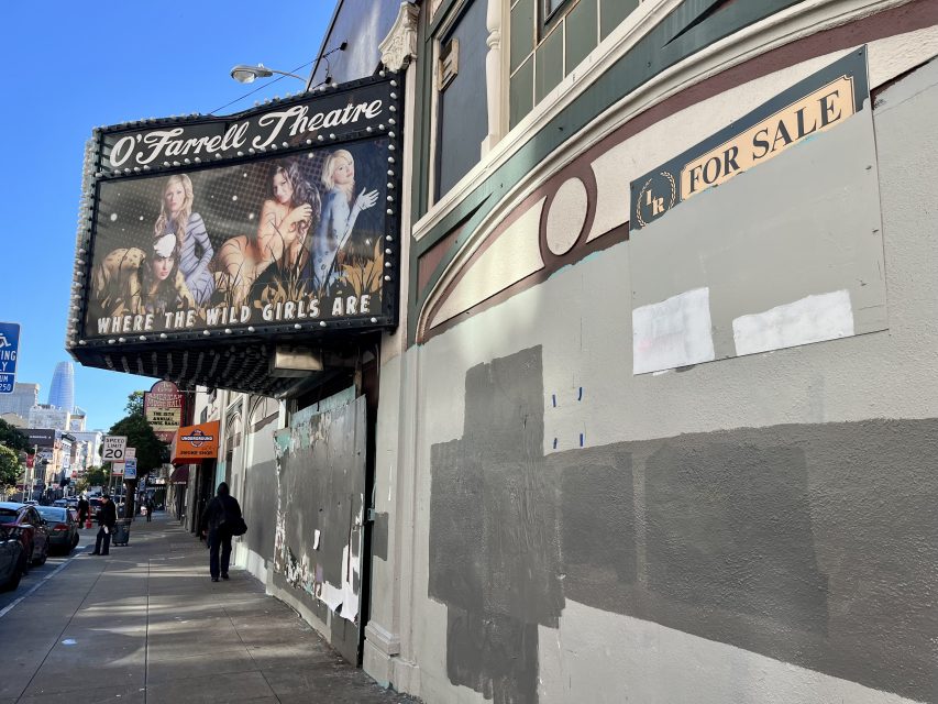 The O'Farrell Theatre marquee reads "Where the Wild Girls Are"; the building has a "For Sale" sign and gray patches on the wall. People walk by on the sidewalk.