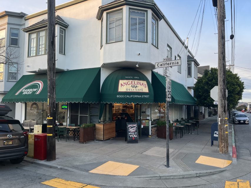 Street view of Angelina’s Deli Cafe with a green awning, outdoor seating, and a sign listing the address as 6000 California Street at a street corner.