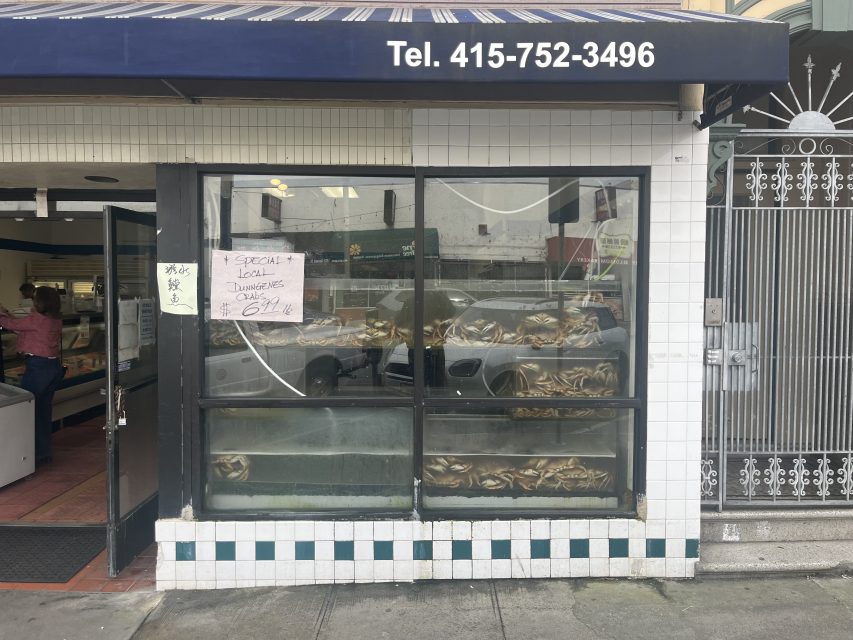 A seafood storefront with live crabs displayed in the window and hand-written signs advertising crabs for $6.99 a pound.