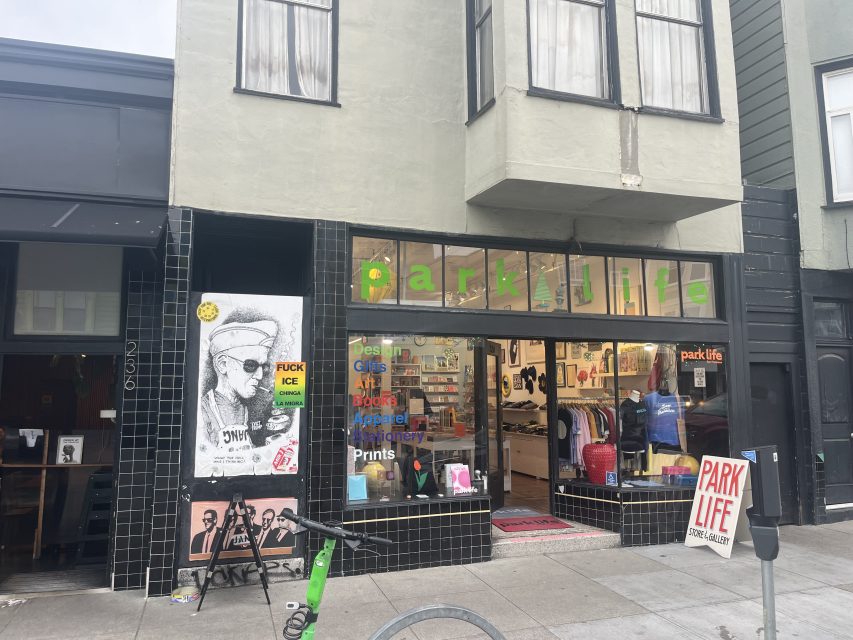 Storefront of "parks life" with a glass display showing art, books, and clothing. A poster and graffiti are visible on the black-tiled exterior wall next to the entrance.