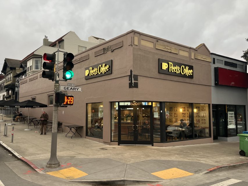 Corner view of a Peet's Coffee shop at dusk with customers inside, outdoor seating, and a traffic light at the intersection of Geary Blvd and 16th Ave.