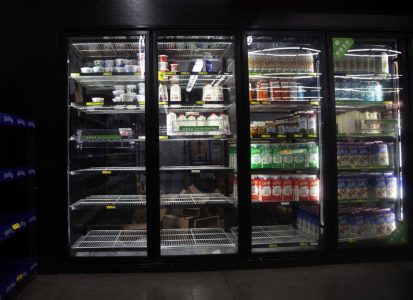 Glass-door refrigerator at a grocery store with mostly empty shelves, displaying limited dairy and juice products.