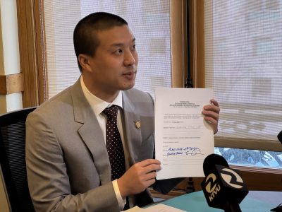 A man in a gray suit holds up and displays a signed document during a press conference, with a microphone labeled KTVU in the foreground.