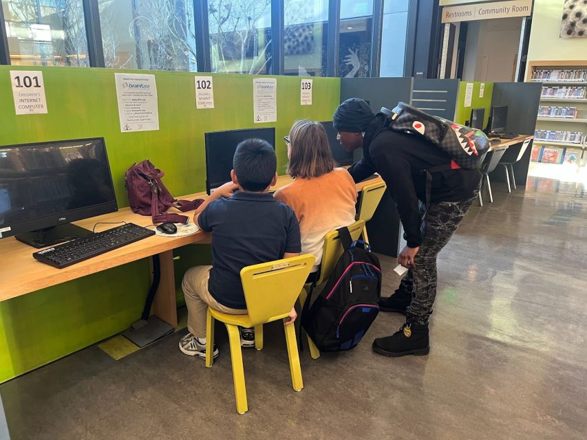 A group of kids sitting at a desk looking at computers.