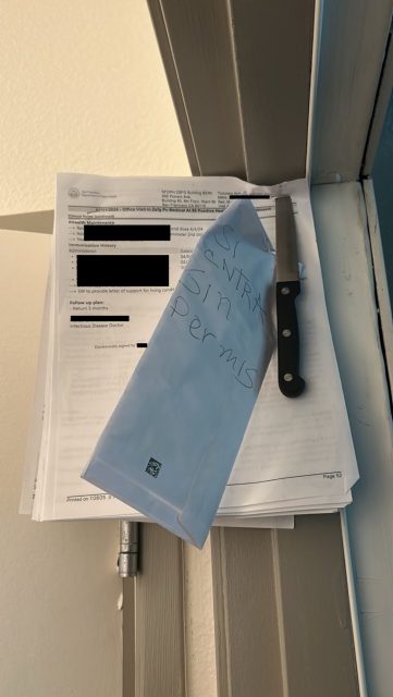 A stack of official documents with redacted text, an envelope labeled "SI ENTRA SIN PERMIS," and a kitchen knife placed on top, all resting on a door hinge.