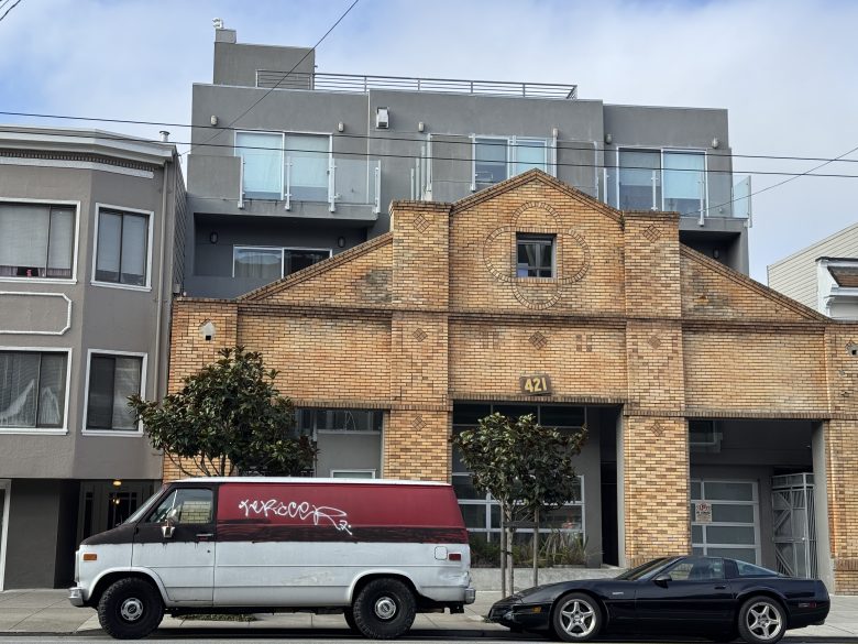 A brick building with modern glass balconies stands behind a red-and-white van with graffiti and a black sports car parked on the street.