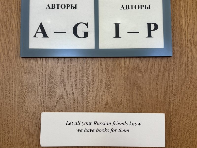 Sign on a wooden wall reads, "Let all your Russian friends know we have books for them," below another sign organizing authors alphabetically by Russian letters.