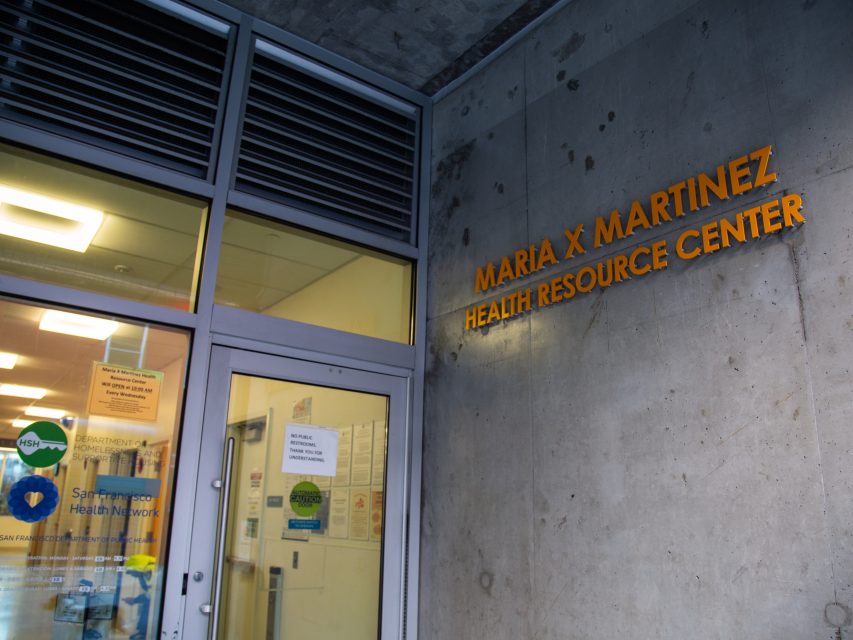 Entrance to the María X Martinez Health Resource Center, with glass doors and signage on a concrete wall.