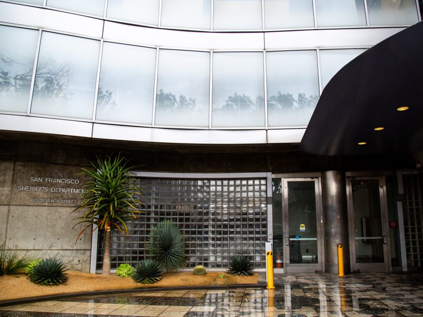 Entrance to the San Francisco Sheriff’s Department at 425 Seventh Street, featuring glass blocks, desert plants, and wet pavement.