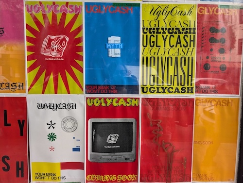 A grid of colorful posters with bold text, including phrases like "UGLYCASH," "COMING SOON," and "YOUR BANK WON'T DO THIS," displayed on a wall.