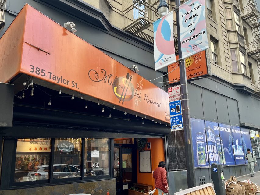 An orange awning above a restaurant entrance at 385 Taylor St. A person stands outside. A sign above reads, "The revolution is indeed inside and it's transgender.