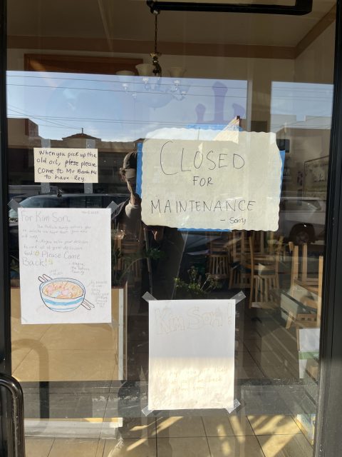 Glass door with handwritten signs, including one reading โClosed for maintenance sorryโ; empty restaurant and wooden chairs visible inside.