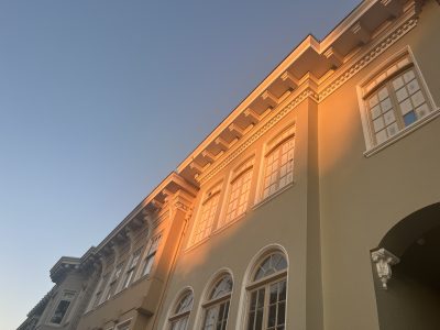 A beige building with large windows is illuminated by warm sunlight, set against a clear blue sky.