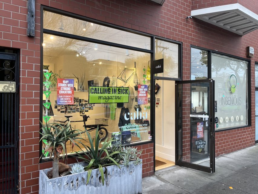 Street view of a storefront with large windows displaying posters, plants in front, and an open door. The sign reads "caha" and "CALLING IN SICK magazine.