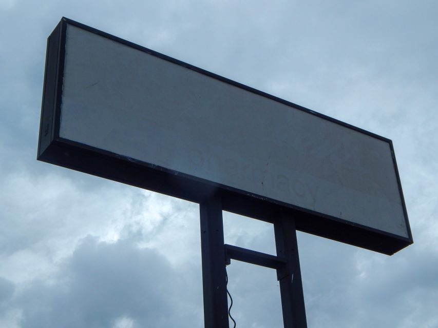 A large, empty rectangular sign stands on two metal poles against a cloudy sky.