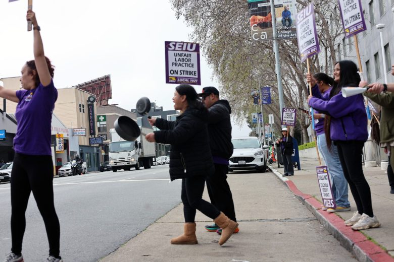 A group of people on a city sidewalk hold SEIU strike signs and bang pots, protesting unfair labor practices.