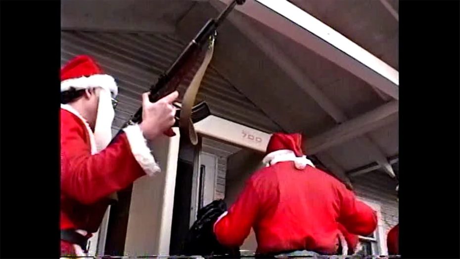 Two people dressed in Santa Claus costumes, one holding a rifle, stand near the entrance of a building numbered 790.