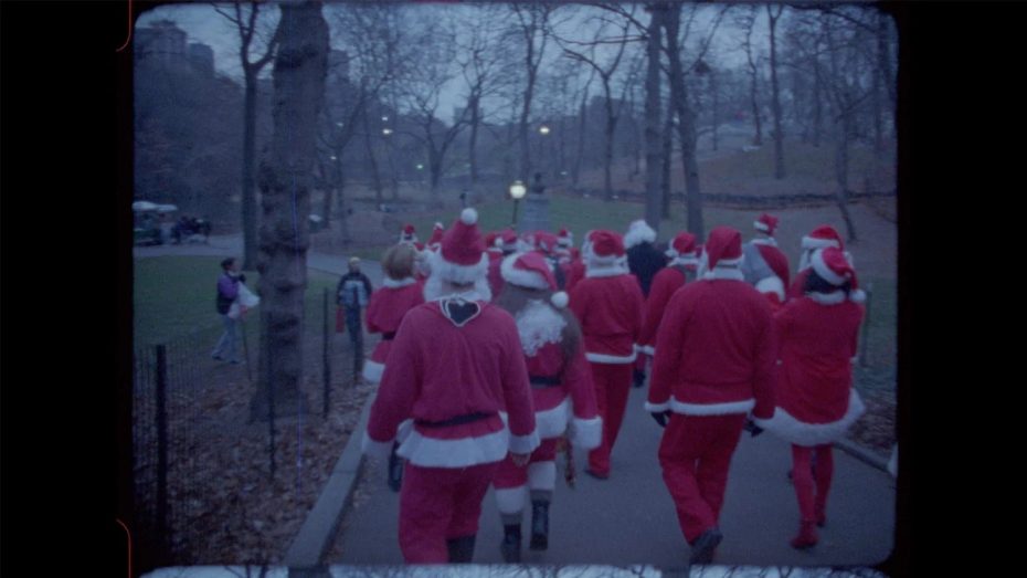A group of people dressed in Santa Claus costumes walk along a paved path in a park with leafless trees.