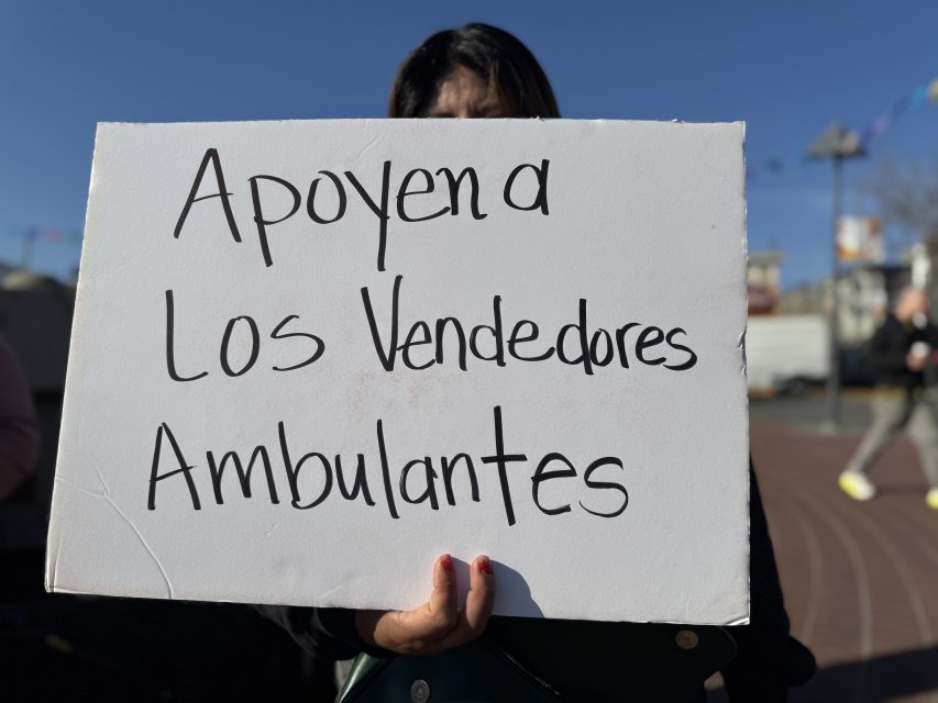 Person holding a white sign with black handwritten text that reads, "Apoyen a los vendedores ambulantes," which translates to "Support street vendors.