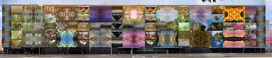 A large building facade featuring a grid of colorful, abstract and mirrored nature-themed photographic panels above street level.
