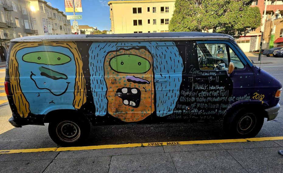 A van parked on a city street features colorful cartoon faces and handwritten messages painted on its side.