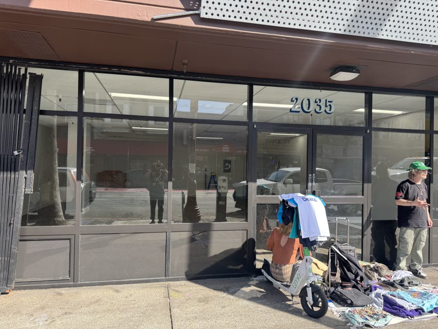 Street view of a glass storefront at 2035 with reflections in the windows; two people stand outside, with clothes and personal items laid out on the sidewalk.