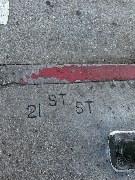 Sidewalk concrete reads "21 ST ST" near a red-painted curb and a metal pole at the bottom right corner.