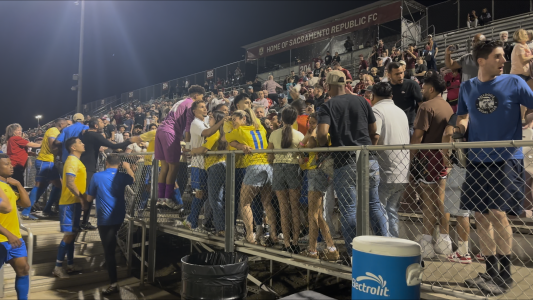 Soccer players in yellow and blue uniforms celebrate with cheering fans by the stands at a night game, with a "Home of Sacramento Republic FC" sign in the background.