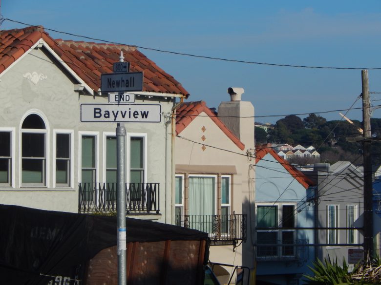 Street signs for Newhall Street and Bayview with “end” indicated, set against residential houses with tiled roofs and a clear sky in the background.