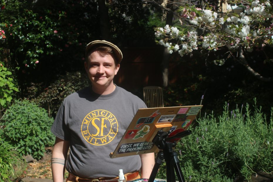 A person wearing a "Municipal Railway" T-shirt and hat stands outdoors beside an easel, surrounded by greenery and blooming trees.