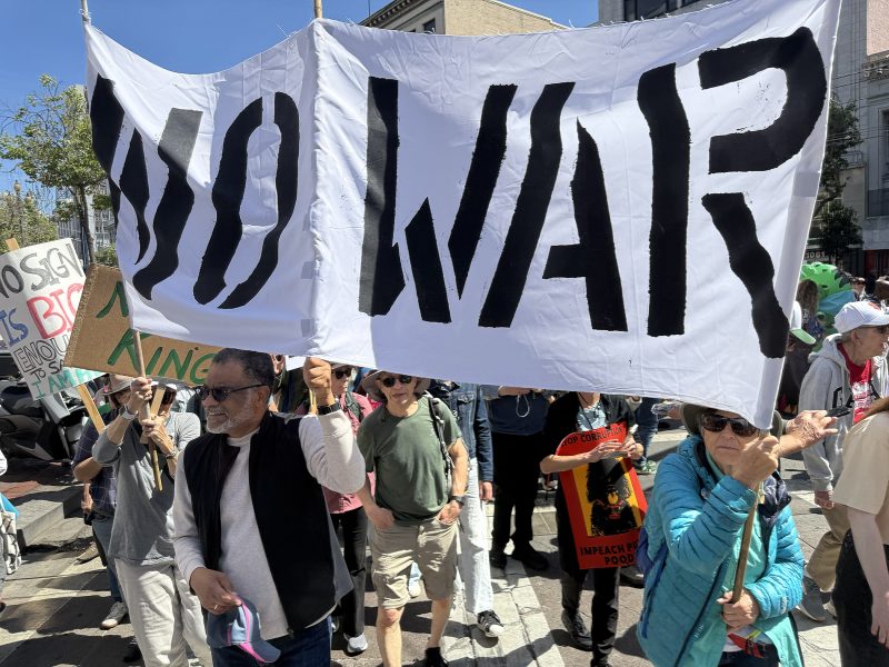 A group of people at a protest holding a large white banner with "NO WAR" written in bold black letters.