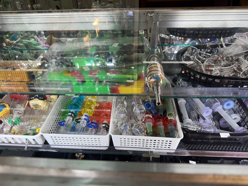 A display case filled with various glass pipes, colorful glass items, and smoking accessories organized in trays and baskets.