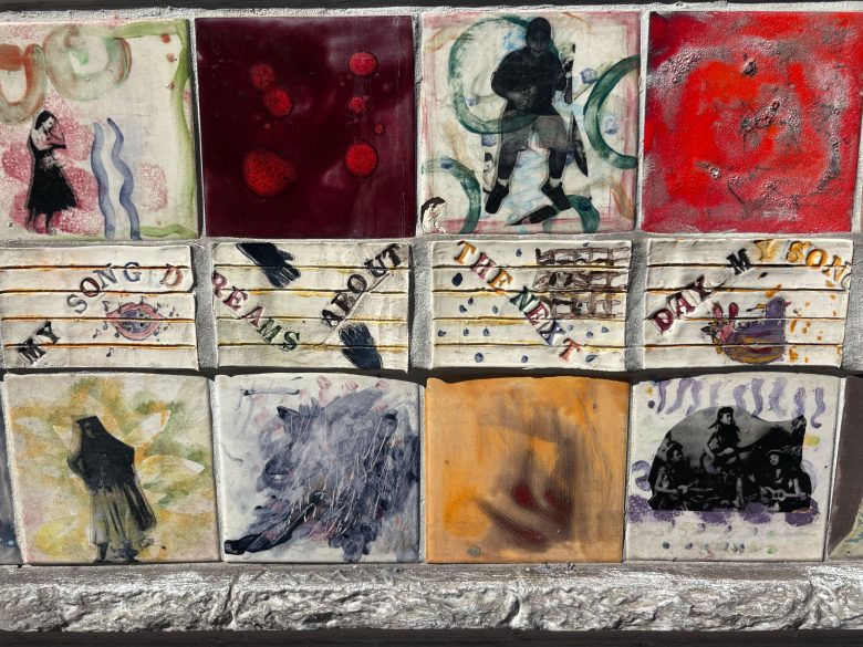 A mosaic of twelve colorful tiles, each with abstract designs, musical notes, and human silhouettes, set into a stone frame.