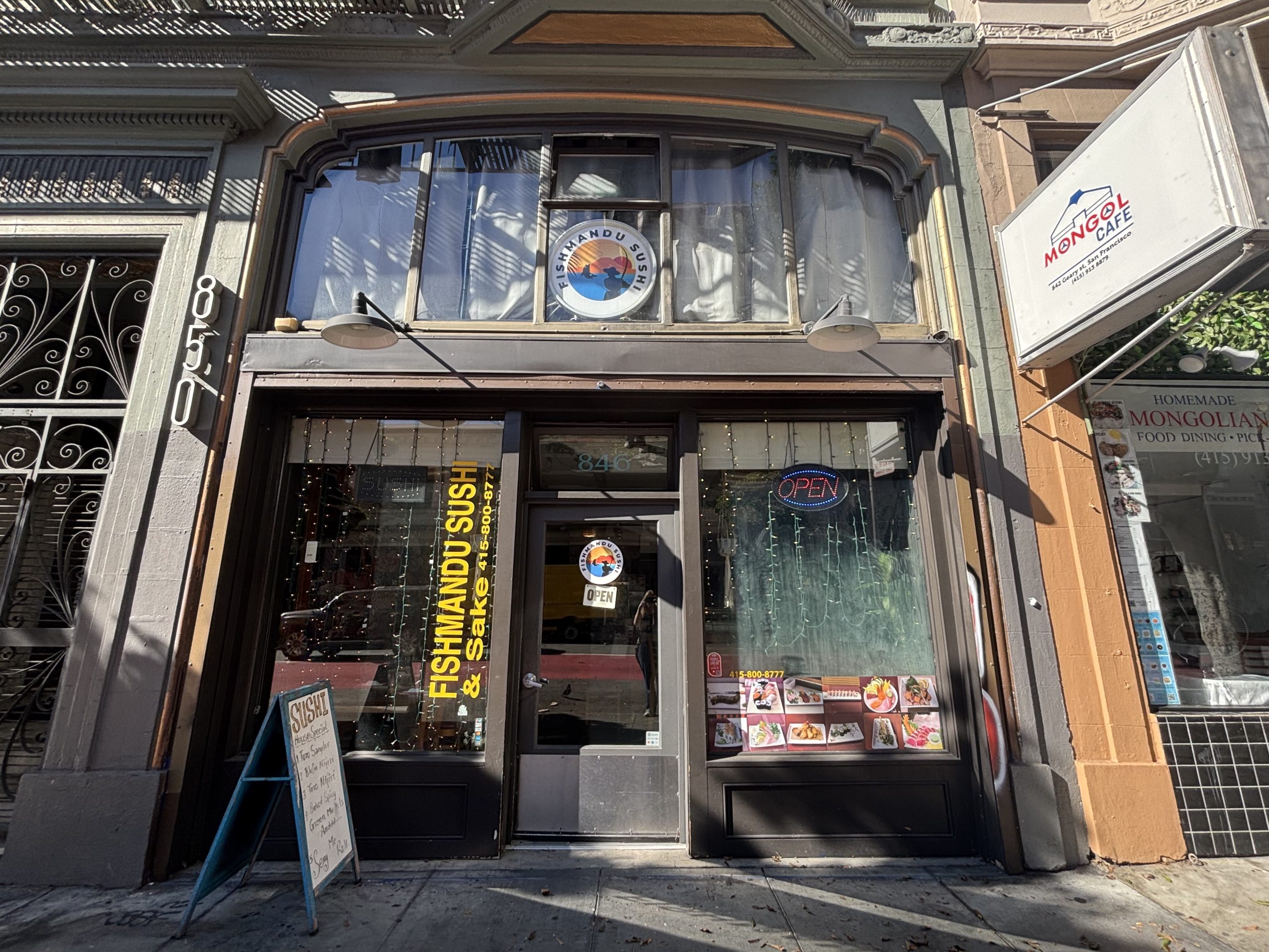 Street view of a restaurant named "Fishmandu Sushi & Shikhar Bar & Grill" with an "OPEN" sign and menu photos displayed on the glass door and window.