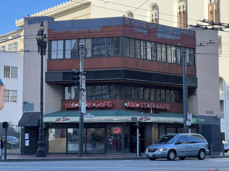 A corner building houses All Star Cafe with large red signs, streetlights, and a parked minivan in front on a sunny day.