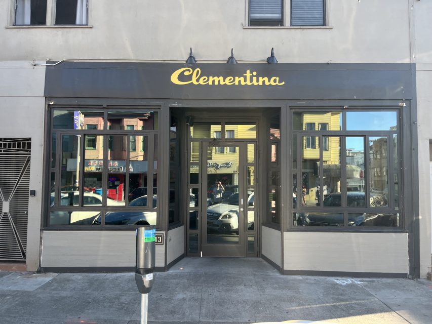 Storefront of a business named "Clementina" with large windows and a glass door, located on a city street with parked cars and buildings reflected in the windows.