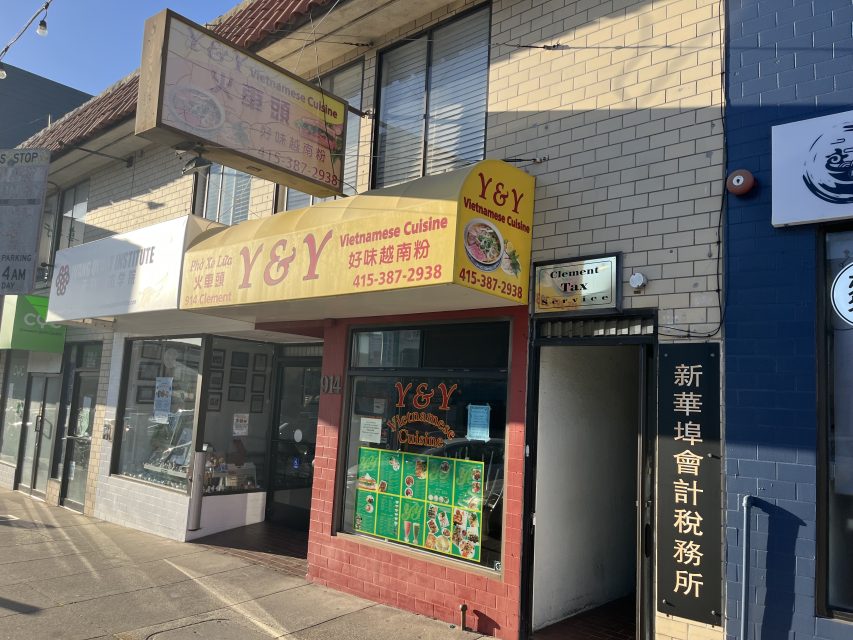 Storefront of Y&Y Vietnamese Cuisine with yellow signage, menu photos in the window, and an adjacent doorway displaying signs with Chinese characters.
