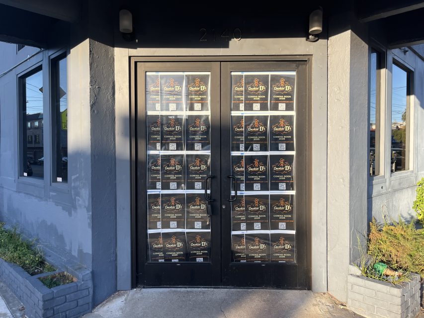 Double glass doors are covered with multiple identical posters displaying event or business information; the number 2140 is above the doors. Gray building exterior and planter boxes are visible.
