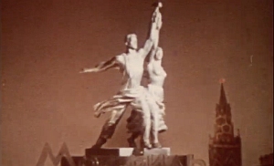 A metal statue of a man and woman holding a hammer and sickle, with a spire visible in the background.