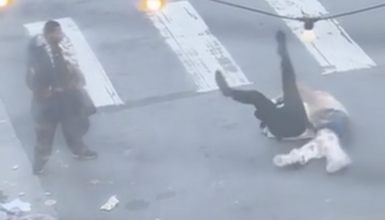 Two people are falling or wrestling on a street crosswalk near Lurie while another person stands nearby watching.