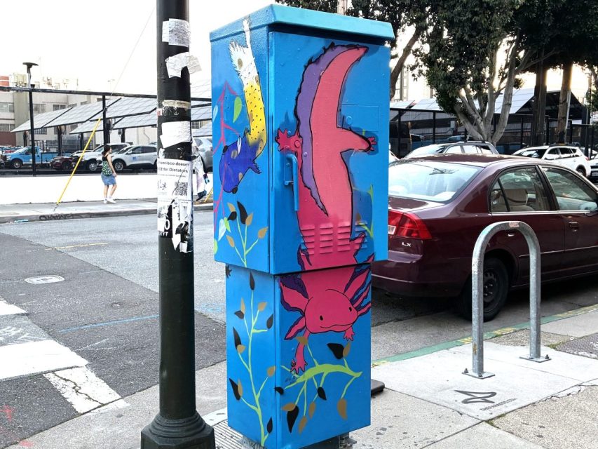 A utility box painted blue features colorful axolotls swimming among plants on a city sidewalk next to a parked maroon car and a pole with flyers.