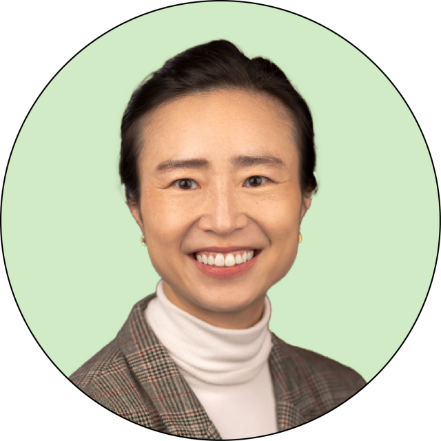 Woman with dark hair pulled back, wearing a plaid blazer and white turtleneck, smiling at the camera against a light green background.