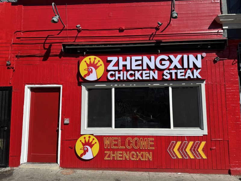 A red storefront with a sign reading "ZHENGXIN CHICKEN STEAK" and "WELCOME ZHENGXIN" beneath a logo featuring a chicken head.
