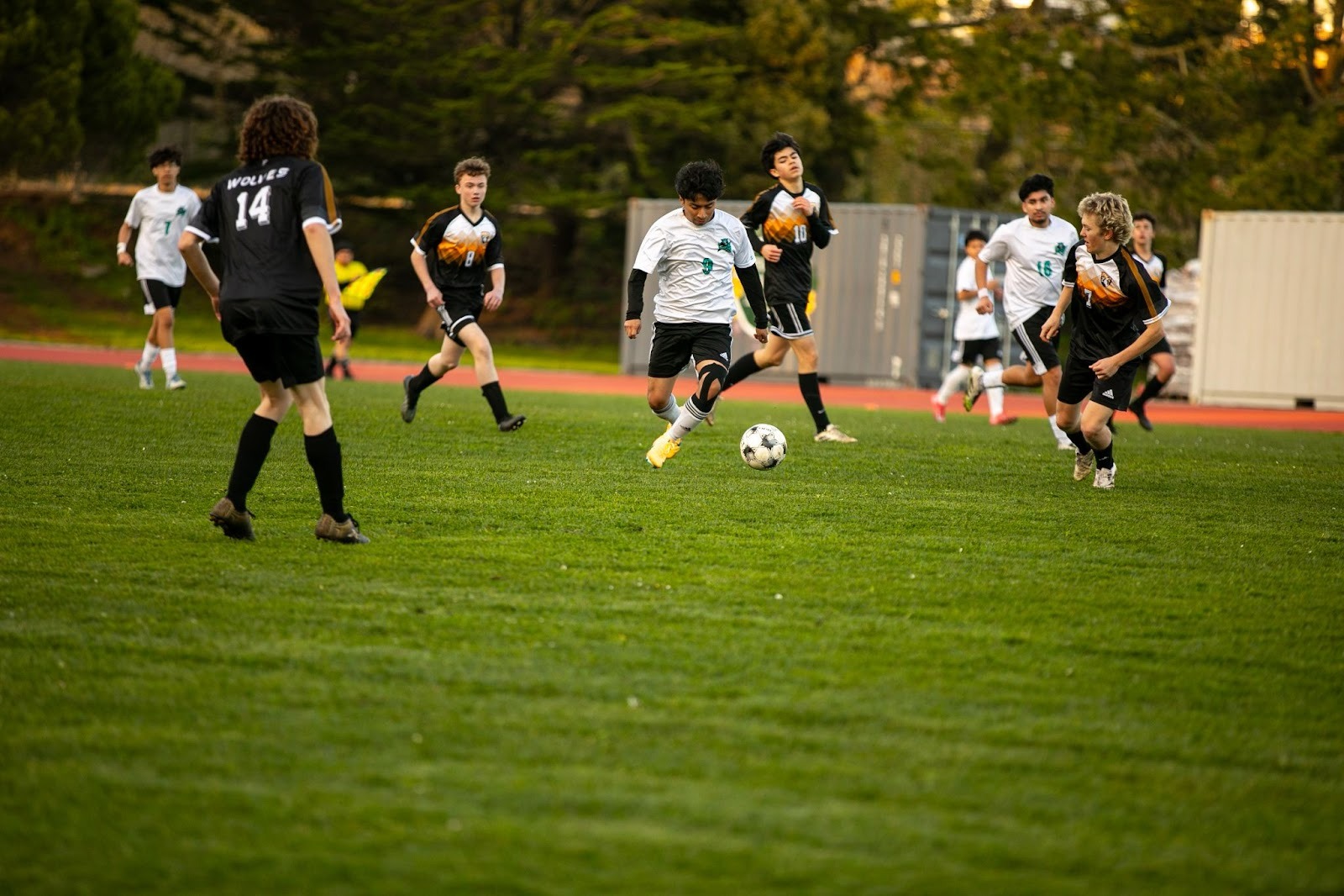 A group of teenage boys play an intense game of soccer on a grassy field, with players in black and white uniforms running toward the ball.